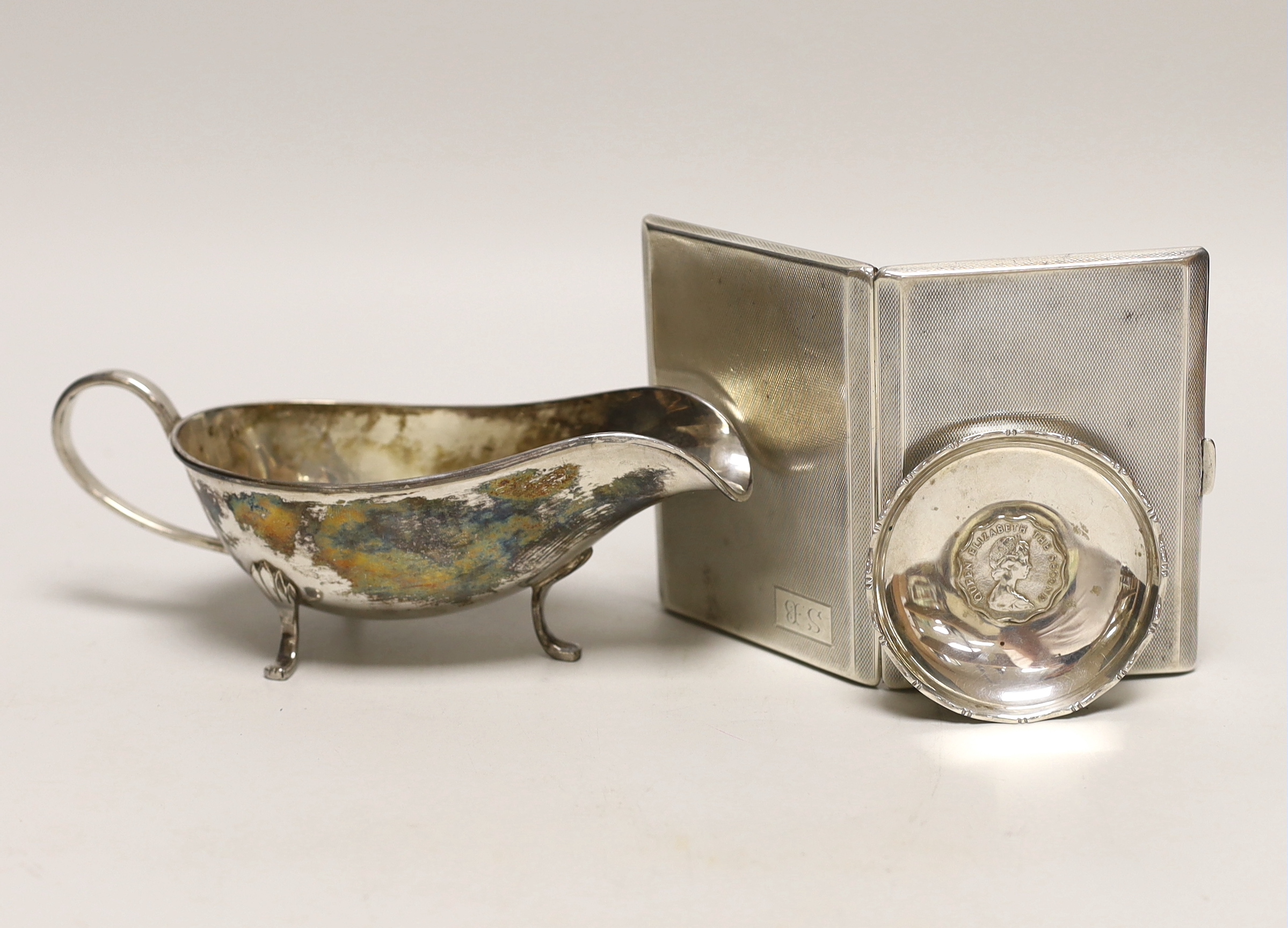 A George V engine turned silver cigarette case, 11.3cm a white metal sauceboat and a Wai Kee sterling pin dish.